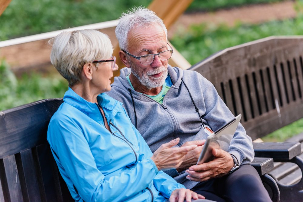 2 people sitting on an outside bench and looking at a tablet