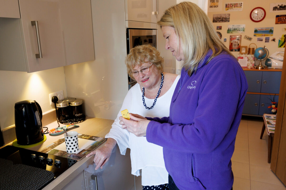Vision PK Rehab worker Debi pictured with service user Linda and a liquid level indicator showing her how it works